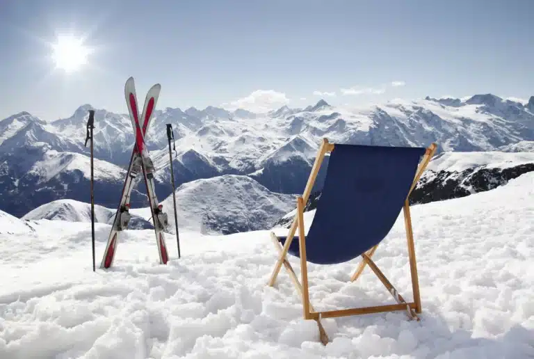 Folding chair in the snow with crossed skis next to it